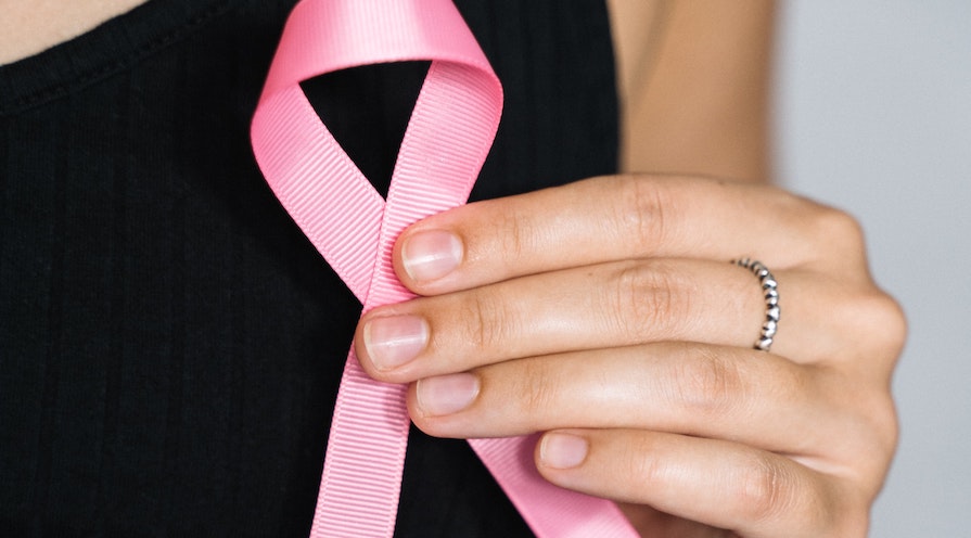 Hand håller i rosa bandet ring för att uppmärksamma bröstcancer